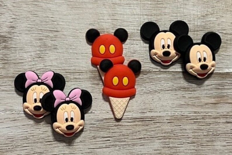 May include: Four colorful cartoon character face charms, two Mickey Mouse, one Minnie Mouse, and one Mickey Mouse ice cream cone. The charms are made of silicone and have a glossy finish.