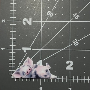 May include: A pink pig cartoon character laying on its side with its legs in the air. The pig has a pink nose and black eyes.