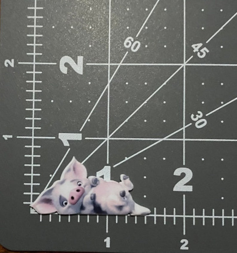 May include: A pink pig cartoon character laying on its side with its legs in the air. The pig has a pink nose and black eyes.