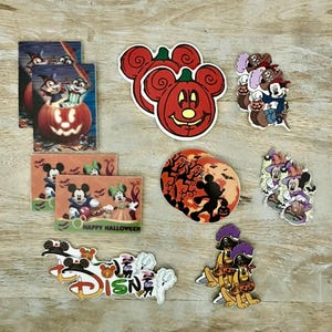 Puede incluir: Una colección de pegatinas de Disney con temática de Halloween con Mickey Mouse, Minnie Mouse, Goofy y una calabaza. Las pegatinas están sobre una superficie de madera.