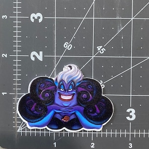 K&ouml;nnte beinhalten: Ein lila und schwarzer Ursula-Aufkleber aus dem Disney-Film Die kleine Meerjungfrau. Ursula ist eine Meereshexe mit langen, wei&szlig;en Haaren und einem b&ouml;sen L&auml;cheln. Sie ist von Tentakeln umgeben.