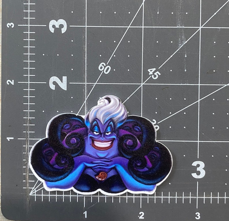 K&ouml;nnte beinhalten: Ein lila und schwarzer Ursula-Aufkleber aus dem Disney-Film Die kleine Meerjungfrau. Ursula ist eine Meereshexe mit langen, wei&szlig;en Haaren und einem b&ouml;sen L&auml;cheln. Sie ist von Tentakeln umgeben.