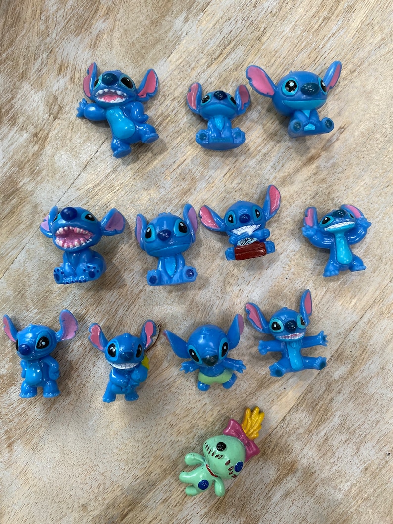 May include: A collection of 12 blue Stitch figurines, featuring various poses and expressions. One figurine is green and has a yellow antenna.