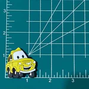 May include: A yellow cartoon car charm with a smiling face and black wheels. The charm is made of rubber and is about 2 inches long.