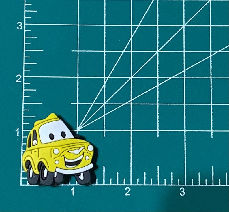 May include: A yellow cartoon car charm with a smiling face and black wheels. The charm is made of rubber and is about 2 inches long.