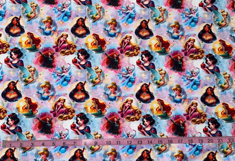 May include: Fabric with a repeating pattern of cartoon princesses, fairies, and other characters on a colorful, watercolor-style background. The princesses include Snow White, Cinderella, and others. A pink measuring tape is at the bottom.