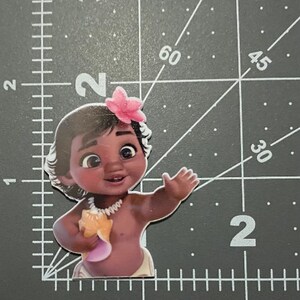 May include: A brown-skinned baby with dark hair and brown eyes is wearing a pink flower in her hair and a white necklace. She is holding a seashell in her right hand and is wearing a white diaper.