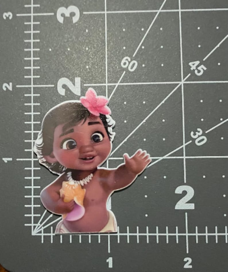 May include: A brown-skinned baby with dark hair and brown eyes is wearing a pink flower in her hair and a white necklace. She is holding a seashell in her right hand and is wearing a white diaper.