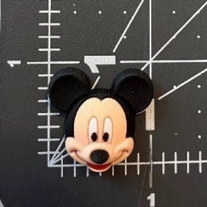 May include: A black and red cartoon character with large ears and a big smile. The character is Mickey Mouse.