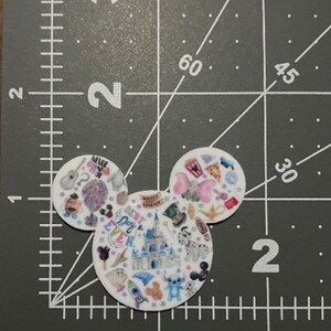 Puede incluir: Forma de cabeza de Mickey Mouse blanca con una variedad de personajes e iconos de Disney coloridos, incluidos Mickey Mouse, Minnie Mouse, Stitch y el castillo de Disney. El texto "Best Day Ever" es visible en el centro de la imagen.