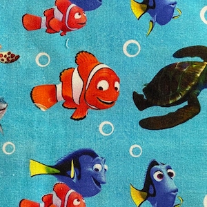 May include: A blue and orange fabric with a repeating pattern of cartoon fish and a sea turtle. The fish are blue with yellow fins and orange with white stripes. The turtle is brown with a green shell.