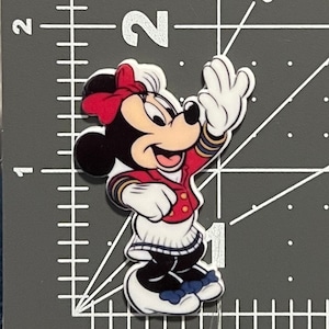 May include: A red, white, and blue Minnie Mouse character wearing a sailor outfit with a red bow. She is waving with her right hand and smiling.