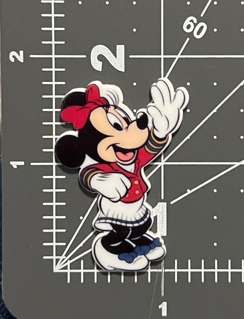 May include: A red, white, and blue Minnie Mouse character wearing a sailor outfit with a red bow. She is waving with her right hand and smiling.