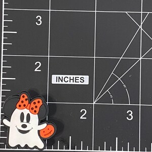 K&ouml;nnte beinhalten: Ein Halloween-Motiv-Charm mit einem Cartoon-Geist mit Minnie-Maus-Ohren und einer Schleife. Der Geist ist wei&szlig; mit einem l&auml;chelnden Gesicht und h&auml;lt einen orangefarbenen K&uuml;rbis. Der Charm ist etwa 2,5 cm gro&szlig;.