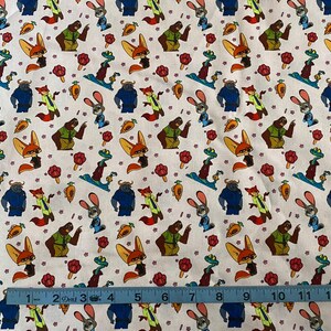 Pode incluir: Tecido branco com um padr&atilde;o repetido de personagens de desenhos animados, incluindo uma raposa, um coelho, um urso e outros animais. O design tamb&eacute;m apresenta cenouras e flores. Uma r&eacute;gua azul mede o tecido.