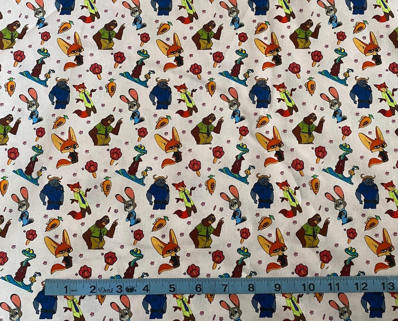 Pode incluir: Tecido branco com um padr&atilde;o repetido de personagens de desenhos animados, incluindo uma raposa, um coelho, um urso e outros animais. O design tamb&eacute;m apresenta cenouras e flores. Uma r&eacute;gua azul mede o tecido.