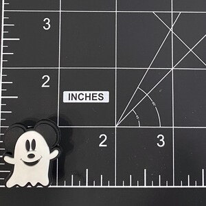 K&ouml;nnte beinhalten: Ein schwarz-wei&szlig;er Mickey Mouse Geister-Charm. Der Charm befindet sich auf einer schwarzen Oberfl&auml;che mit wei&szlig;en Rasterlinien und dem Wort "INCHES". Der Charm ist etwa 5 cm hoch.