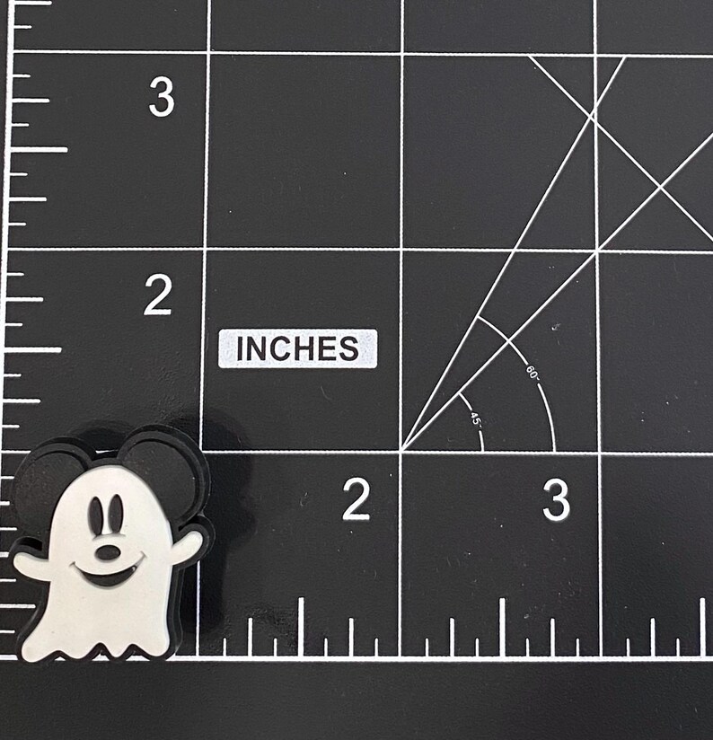 K&ouml;nnte beinhalten: Ein schwarz-wei&szlig;er Mickey Mouse Geister-Charm. Der Charm befindet sich auf einer schwarzen Oberfl&auml;che mit wei&szlig;en Rasterlinien und dem Wort "INCHES". Der Charm ist etwa 5 cm hoch.
