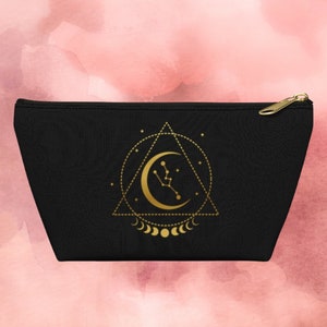 May include: Black canvas zippered pouch with a gold design of a crescent moon, stars, and a geometric triangle pattern.