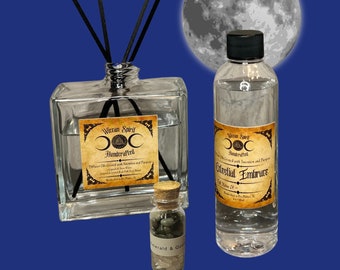 May include: Two glass bottles of room diffuser oil with black sticks and a small glass bottle of crystals. The bottles have labels that say "Witchcraft Spirit Handcrafted" and "Celestial Embrace". The bottles are in front of a full moon.