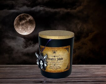 May include: A black candle in a glass jar with a bamboo lid, featuring a label that reads Hecate's Moon, 9oz / 255g. A purple string holds a black and white charm depicting a three-faced figure attached to the front of the candle jar.