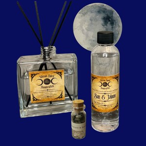 May include: A set of three glass bottles with labels that say "Witcan Spirit Handcrafted" and "Sun & Moon Full Moon Of." The bottles are filled with clear liquid and have black sticks in the larger bottle. The bottles are on a blue background with a watercolor moon.