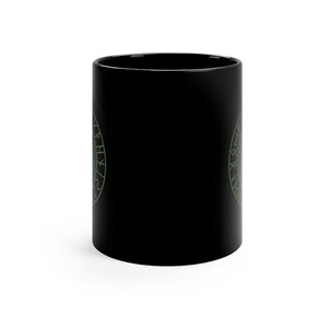 May include: Black ceramic coffee mug with a green circular design featuring a symbol and runes. The design is on both sides of the mug.