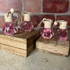 May include: Four pink glass car air fresheners with wooden tops and string hangers. The fresheners are shaped like diamonds and are displayed on two wooden blocks.