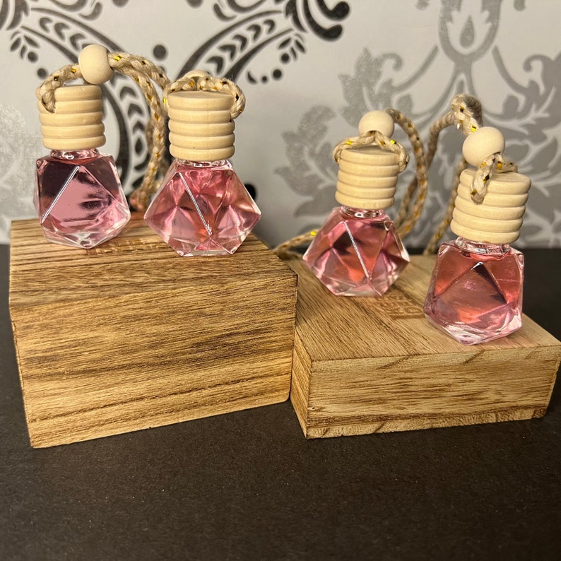 May include: Four pink diamond-shaped glass bottles with wooden caps and gold string attached. The bottles are sitting on two wooden blocks.