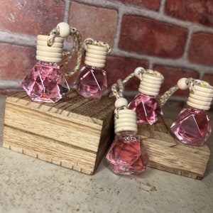 May include: Five pink diamond-shaped glass bottles with wooden lids and gold string hanging from each. The bottles are sitting on a wooden surface.