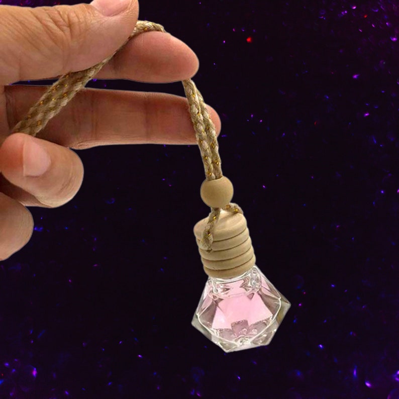 May include: A pink car air freshener in a clear, faceted glass bottle with a wooden cap and a brown cord. The bottle is hanging from a wooden bead.