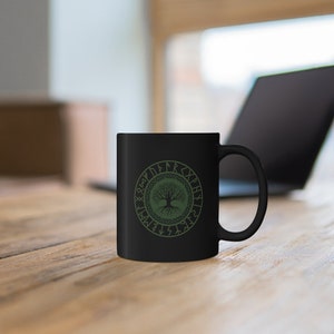May include: Black ceramic mug with a green tree of life design surrounded by a circle of runes.