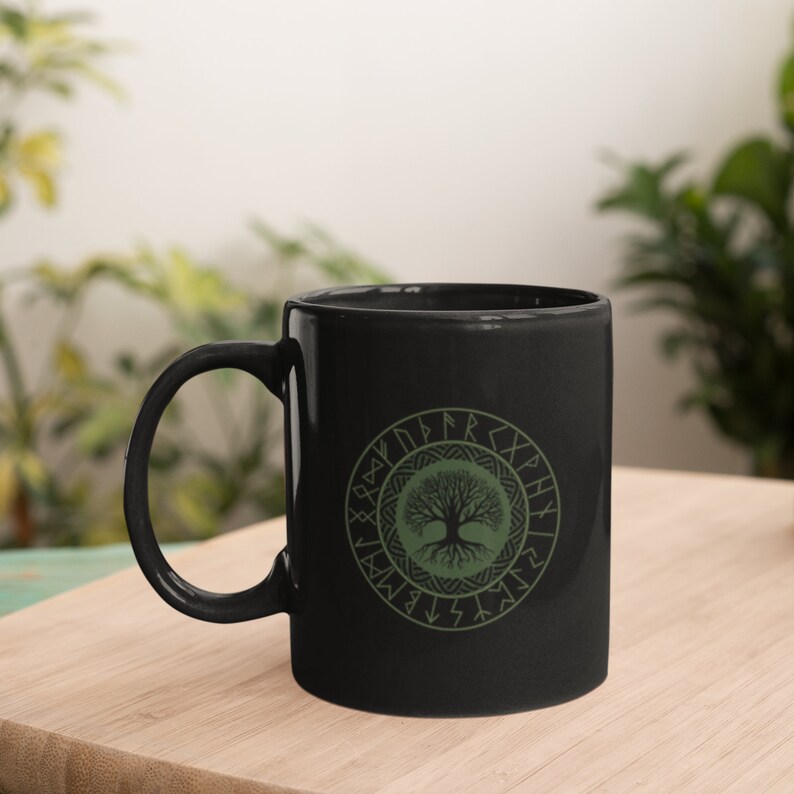 May include: Black ceramic mug with a green tree of life design surrounded by a circle of runes. The runes are in a light green color.