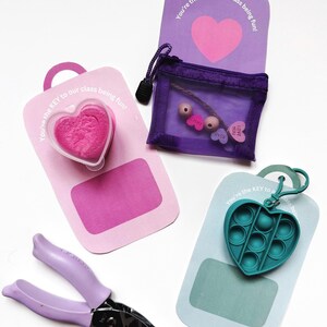 Puede incluir: Tres etiquetas de regalo para el Día de San Valentín con diferentes diseños. La primera etiqueta es morada con un corazón y el texto "You're the KEY to our class being fun!" La segunda etiqueta es rosa con un recipiente en forma de corazón lleno de slime rosa y el texto "You're the KEY to our class being fun!" La tercera etiqueta es azul con un juguete pop-it en forma de corazón verde y el texto "You're the KEY to our class being fun!"