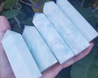 May include: Five light blue crystal points, also known as wands, are arranged in a hand. The points are smooth and polished, with a slight translucence.