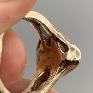 May include: A gold-toned ring with a unique, abstract design. The ring is made of metal and has a textured surface.
