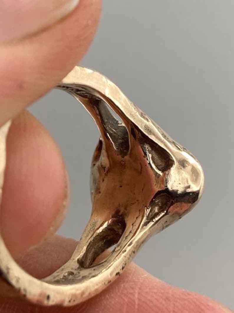 May include: A gold-toned ring with a unique, abstract design. The ring is made of metal and has a textured surface.