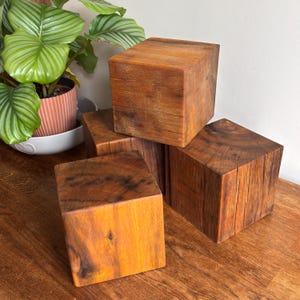 May include: A collection of four solid wooden cubes with a natural brown finish, showcasing visible wood grain patterns and textures. The cubes are arranged in a stacked formation, displaying their square shapes and smooth, flat surfaces.