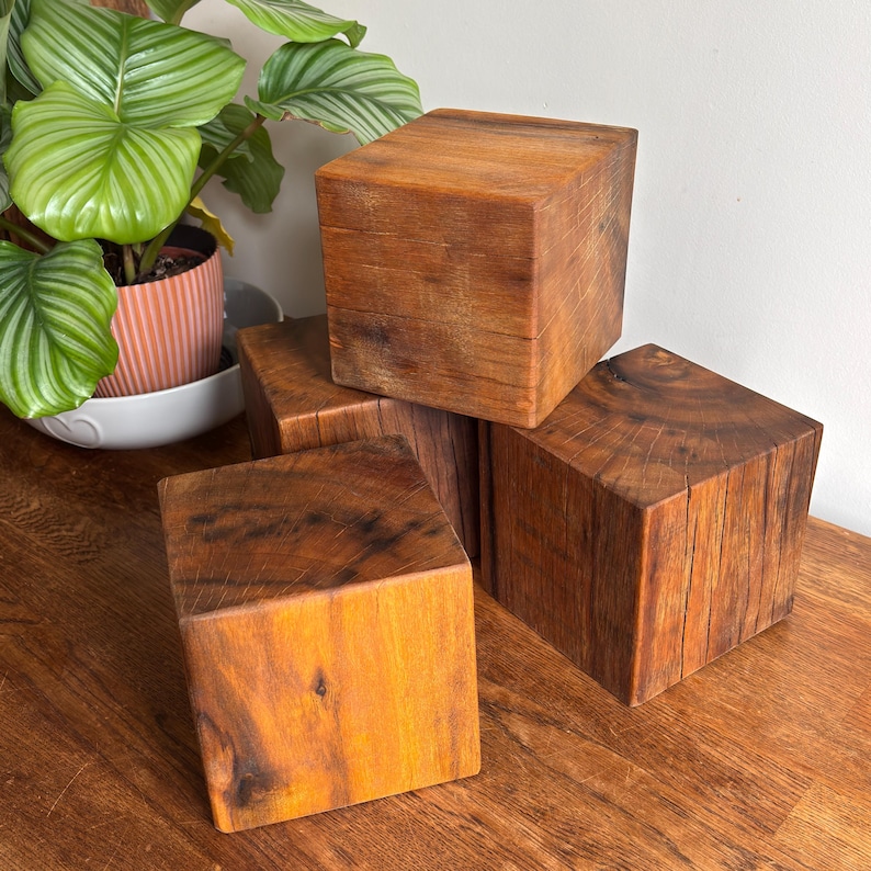 May include: A collection of four solid wooden cubes with a natural brown finish, showcasing visible wood grain patterns and textures. The cubes are arranged in a stacked formation, displaying their square shapes and smooth, flat surfaces.