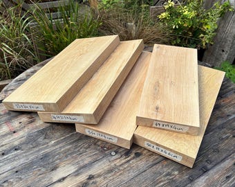 May include: Five rectangular light brown wooden boards with visible wood grain. Each board has a white label with handwritten dimensions in centimeters: 53x24x4 cm, 54x21.5x4 cm, 55x19x4 cm, 49x19x4 cm, and 50x19x4.6 cm. The boards are stacked on a dark surface.