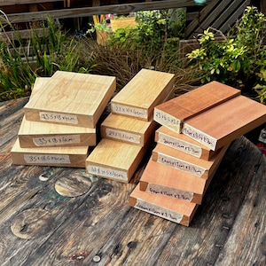May include: A collection of rectangular wooden blocks in varying light and reddish-brown tones. Each block features a white paper label with handwritten metric dimensions in centimetres, such as 23.5x18x4cm, 29x11x4cm, and 40x13x2.7cm, clearly visible on the front edges.