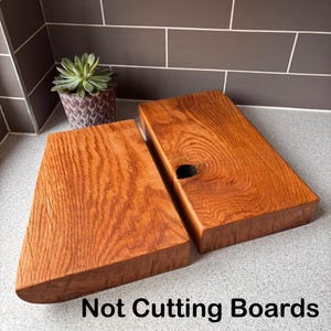May include: Two rectangular wooden blocks with a warm brown finish and visible grain patterns. One block features a dark circular knot. The text "Not Cutting Boards" is printed in black at the bottom of the image, below the two wooden items.