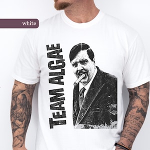 Puede incluir: Una camiseta blanca de manga corta con un estampado gráfico en blanco y negro. El diseño incluye el texto "TEAM ALGAE" en una fuente negrita y desgastada junto al retrato de un hombre con traje y corbata con un puro en la boca.