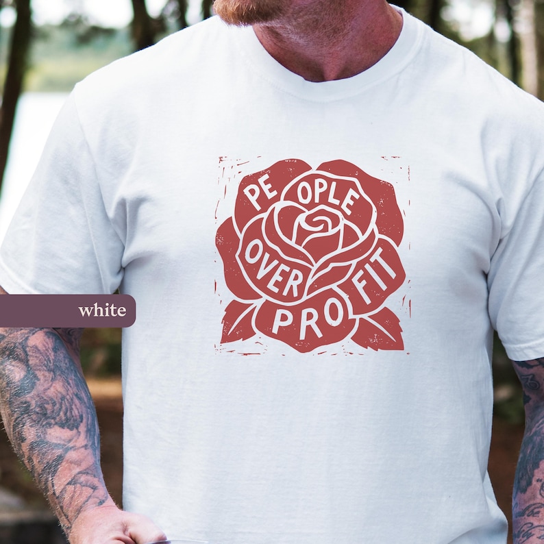 May include: White t-shirt with a red rose graphic. The rose design features the words "People Over Profit" in a circular arrangement. The shirt is made of a soft material and is suitable for casual wear.