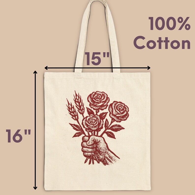 May include: Cream tote bag featuring a red illustration of a hand holding roses and wheat. The bag measures 40.6 cm tall and 38.1 cm wide. The text "100% Cotton" is printed on the upper right.