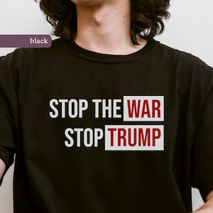 May include: Black t-shirt with the text "STOP THE WAR STOP TRUMP" in white and red lettering. The word "WAR" is in a red box, and "TRUMP" is in a red box. The shirt is a crew neck.