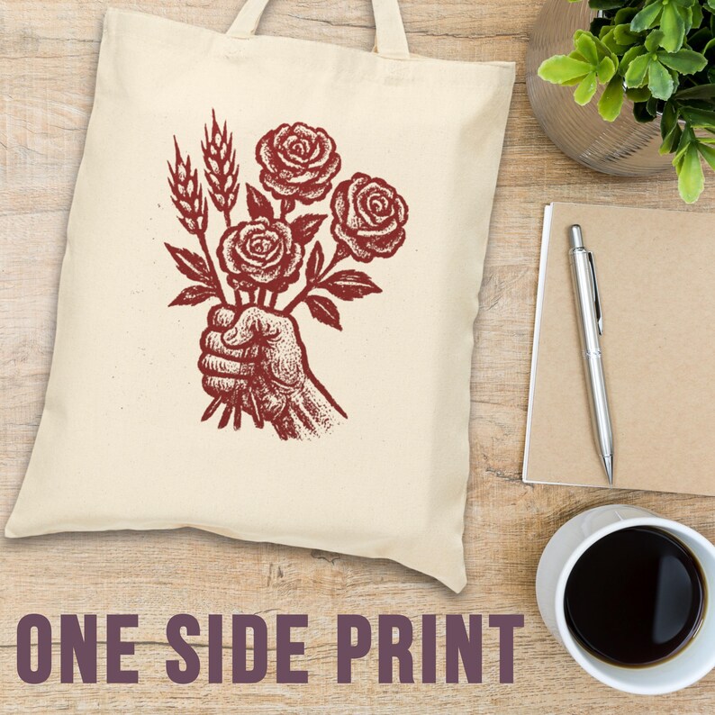 May include: A cream tote bag with a burgundy illustration of a hand holding roses and wheat. The words "ONE SIDE PRINT" are printed in burgundy at the bottom. The bag has two handles.