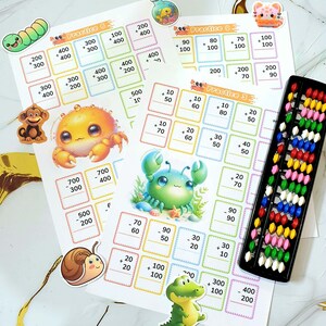 Può includere: Fogli di esercizi di matematica educativa con illustrazioni colorate di creature marine e un abaco. I fogli presentano problemi di addizione e sottrazione con numeri. Simpatici adesivi di un verme, scimmia, granchio, lumaca e alligatore sono sparsi.