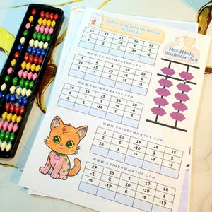 May include: A black abacus with colorful beads sits next to worksheets for addition and subtraction practice. The worksheets feature math problems, the website address www.rainbowmaths.com, and a cartoon cat illustration.