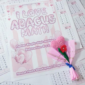 May include: A pink and white educational worksheet titled "I Love Abacus Math" with a crochet heart bouquet. The bouquet includes a pink heart, a red flower, and green stem wrapped in pink paper. Math worksheets are scattered around.